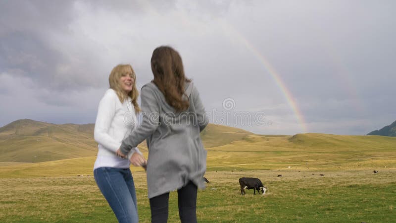 Jonge speelse meisjes dichtbij een pastoraal landschapsgebied met koeien die een selfiefoto met regenboog op achtergrond nemen -