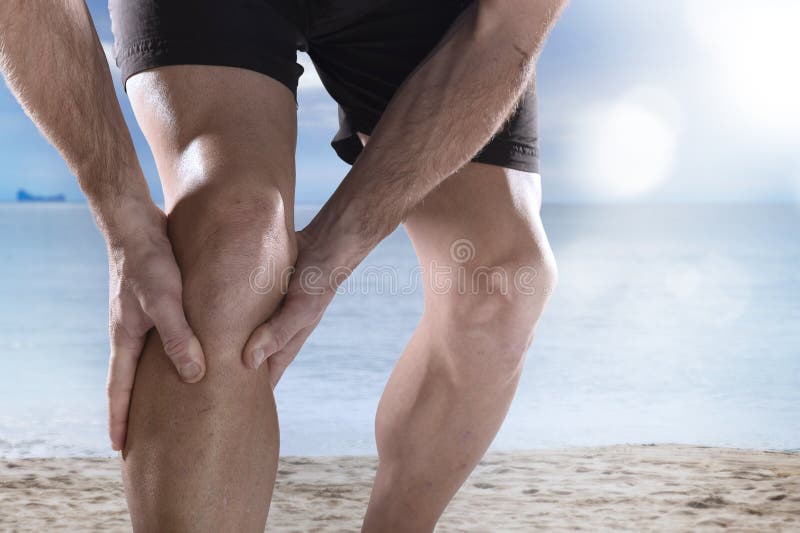 Jonge sportmens die met atletische benen knie in pijn houden die spierverwonding aan het lopen lijden