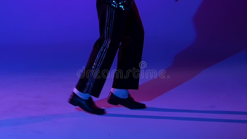 Jonge stijlvolle man danst in stijl Michael Jackson, spotlight op blauwe achtergrond Sluit de benen, langzaam bewegen