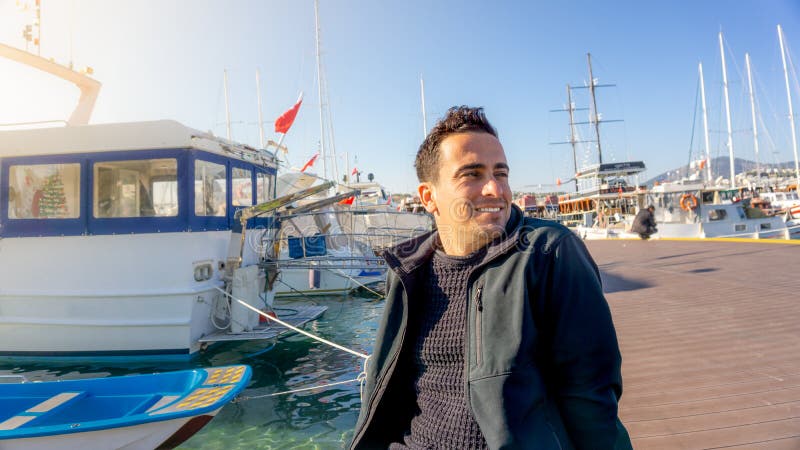 Jonge Turkse toeristenmens die tijdens zonsondergang in Bodrum-jachthaven, Turkije glimlachen Varende boten, zeeman, en duidelijk royalty-vrije stock fotografie Jonge Turkse toeristenmens die tijdens zonsondergang in Bodrum-jachthaven, Turkije glimlachen Varende boten, zeeman, en duidelijk royalty-vrije stock fotografie