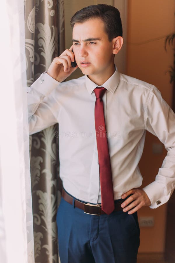 Jonge verontruste zakenman die een mobiele telefoon met behulp van die zich dichtbij het venster in hotelruimte bevinden stock fotografie Jonge verontruste zakenman die een mobiele telefoon met behulp van die zich dichtbij het venster in hotelruimte bevinden stock fotografie