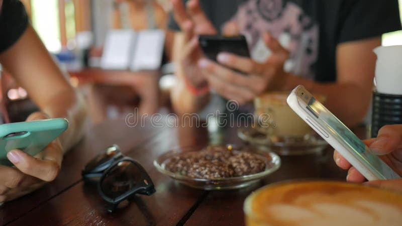 Jonge Vrienden die Mobiele Smartphones-Zitting in Koffiewinkel gebruiken thailand