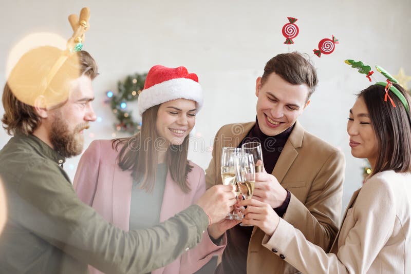 Young cheerful colleagues in xmas headbands clinking with flutes of champagne while toasting for successful work in the next year. Young cheerful colleagues in xmas headbands clinking with flutes of champagne while toasting for successful work in the next year