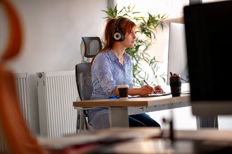 Jonge vrouw die aan de muziek luisteren terwijl het werken aan een computer royalty-vrije stock foto Jonge vrouw die aan de muziek luisteren terwijl het werken aan een computer royalty-vrije stock foto