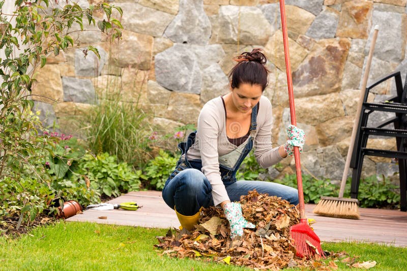 Jonge vrouw die de stapelveranda harken van de bladerenherfst stock foto Jonge vrouw die de stapelveranda harken van de bladerenherfst stock foto