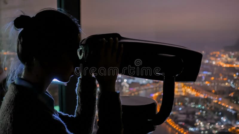 Jonge vrouw die door toeristentelescoop kijken en nachtcityscape onderzoeken royalty-vrije stock afbeelding Jonge vrouw die door toeristentelescoop kijken en nachtcityscape onderzoeken royalty-vrije stock afbeelding