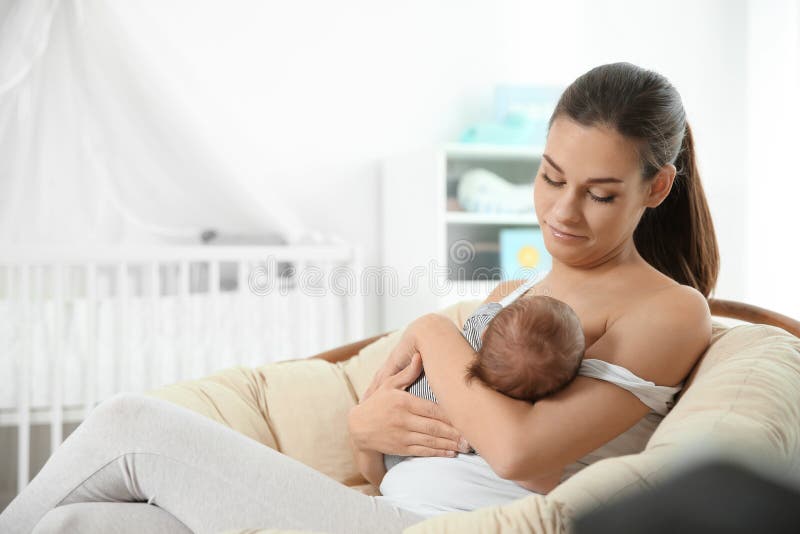 Jonge vrouw die haar baby in kinderdagverblijf de borst geven stock fotografie Jonge vrouw die haar baby in kinderdagverblijf de borst geven stock fotografie
