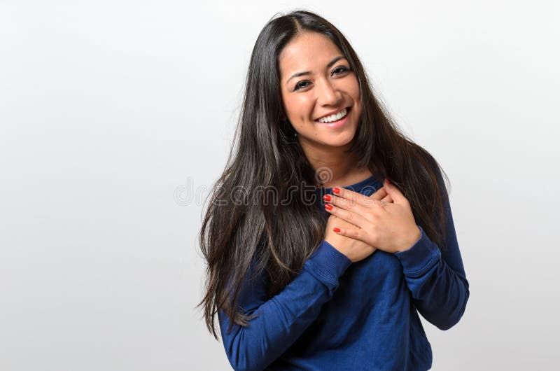 Young woman showing her heartfelt gratitude and thanks clasping her hands to her heart with a pleased smile. Young woman showing her heartfelt gratitude and thanks clasping her hands to her heart with a pleased smile
