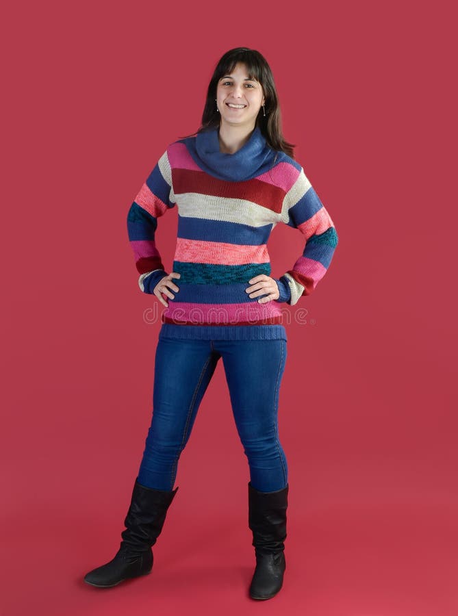 Young woman smiling in a striped sweater on her feet on a magenta background. Caucasian woman with long brunette hair posing in studio. Young woman smiling in a striped sweater on her feet on a magenta background. Caucasian woman with long brunette hair posing in studio.