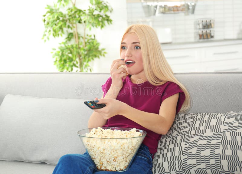 Jonge vrouw die met afstandsbediening en kom popcorn op TV op bank letten stock foto's Jonge vrouw die met afstandsbediening en kom popcorn op TV op bank letten stock foto's