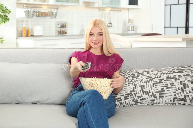 Jonge vrouw die met afstandsbediening en kom popcorn op TV op bank letten royalty-vrije stock foto Jonge vrouw die met afstandsbediening en kom popcorn op TV op bank letten royalty-vrije stock foto