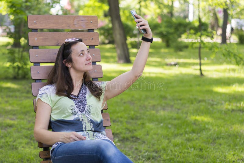 Jonge vrouw die selfie in het park maken Sexy jonge vrouw met lang blond haar die selfie op de zomerdag doen in park Vrolijk meis stock fotografie Jonge vrouw die selfie in het park maken Sexy jonge vrouw met lang blond haar die selfie op de zomerdag doen in park Vrolijk meis stock fotografie