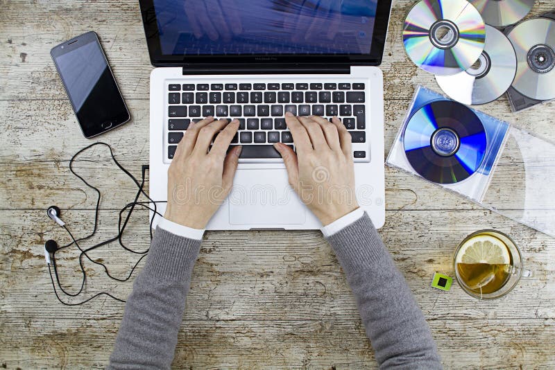 Jonge vrouw die van boven het werken aan laptop op houten lijst schiet die aan muziekcd luistert met een kop thee en een hoofdtel royalty-vrije stock afbeelding Jonge vrouw die van boven het werken aan laptop op houten lijst schiet die aan muziekcd luistert met een kop thee en een hoofdtel royalty-vrije stock afbeelding