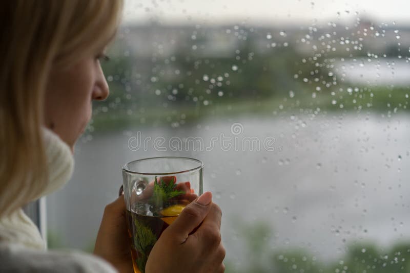 Jonge Vrouw die van haar ochtendthee genieten, die uit het Regenachtige Venster kijken Het mooie romantische onherkenbare meisje royalty-vrije stock foto Jonge Vrouw die van haar ochtendthee genieten, die uit het Regenachtige Venster kijken Het mooie romantische onherkenbare meisje royalty-vrije stock foto