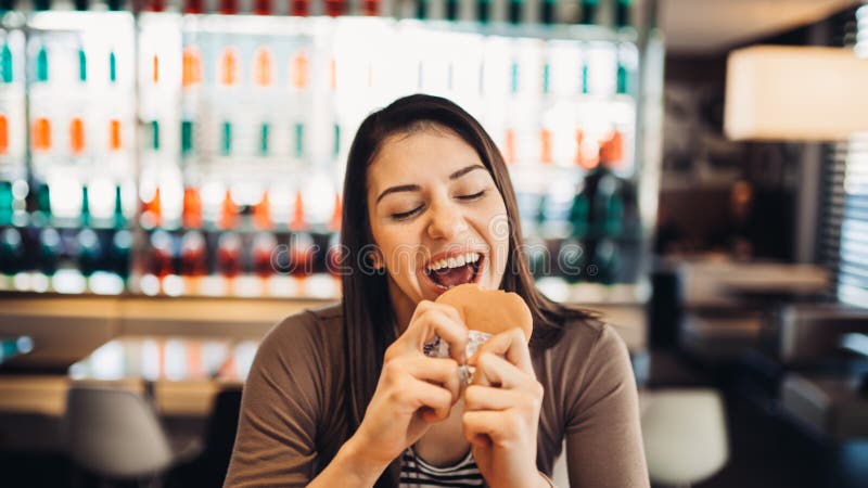 Jonge vrouw die vettige hamburger eten Het hunkeren naar snel voedsel Genietend van schuldig genoegen, die ongezonde kost eten Te