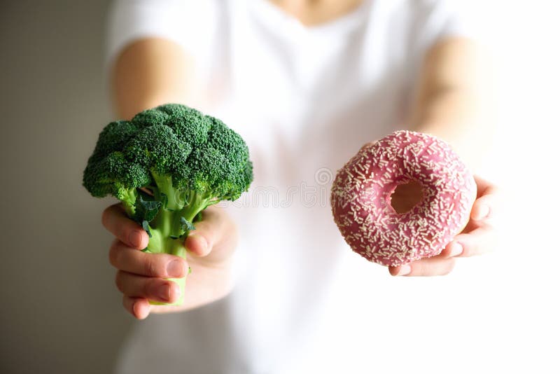 Jonge vrouw die in witte T-shirt tussen broccoli of ongezonde kost, doughnut kiezen Gezonde schone detox die concept eten