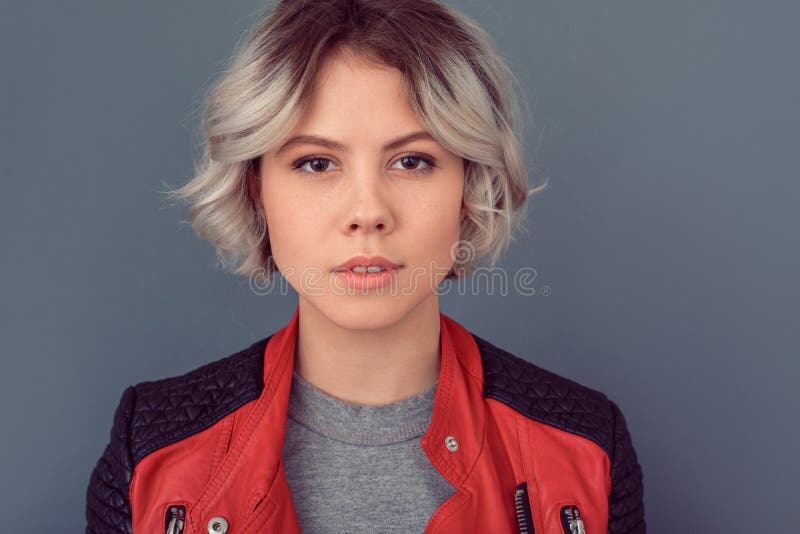 Jonge vrouw die zich in leerjasje bevinden op het grijze close-up van de muursensualiteit stock fotografie Jonge vrouw die zich in leerjasje bevinden op het grijze close-up van de muursensualiteit stock fotografie