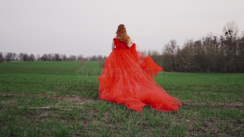 Jonge vrouw in een luxueuze rode kledingslooppas langs het groene gras