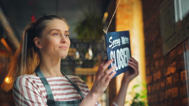 Jonge vrouw het openen koffie die in ochtend zijn wij open teken op voordeur hangt