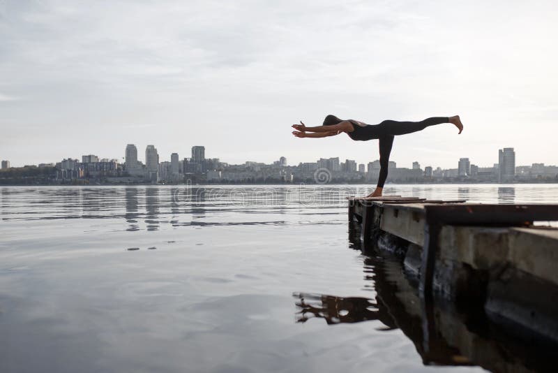 Jonge vrouw het praktizeren yogaoefening bij stille houten pijler met stadsachtergrond Sport en recreatie in stadsstormloop royalty-vrije stock afbeeldingen Jonge vrouw het praktizeren yogaoefening bij stille houten pijler met stadsachtergrond Sport en recreatie in stadsstormloop royalty-vrije stock afbeeldingen