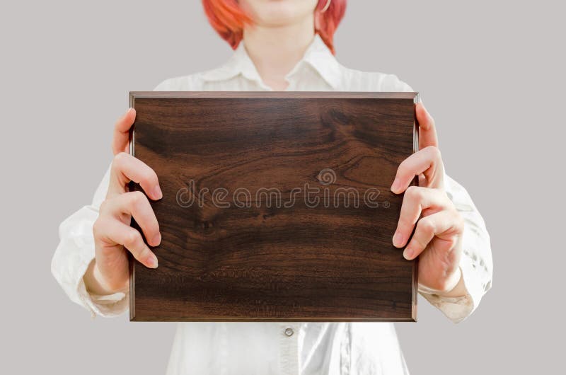 young woman holds a wooden award plaque in her hands in front of her. young woman holds a wooden award plaque in her hands in front of her