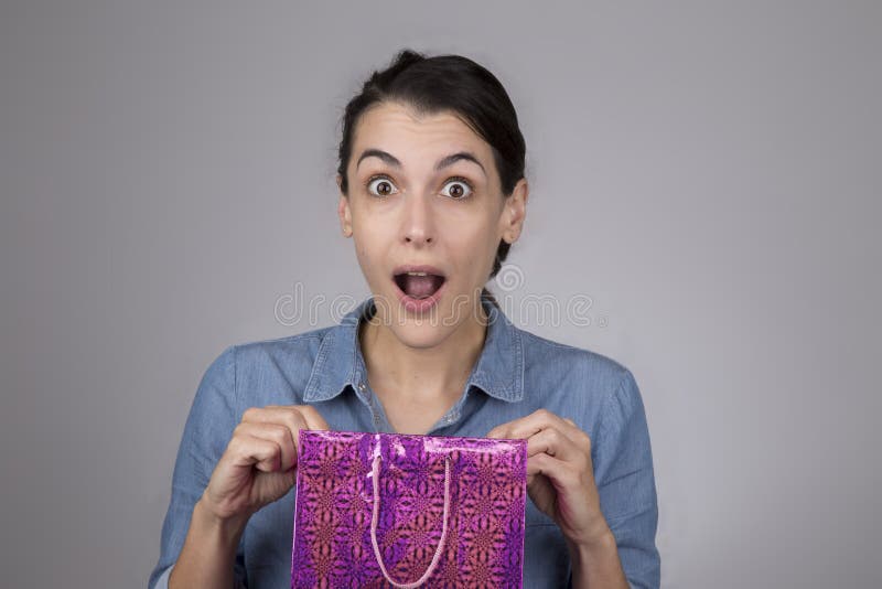 jonge vrouw met verraste uitdrukking op haar gezicht aangezien zij giftzak opent royalty-vrije stock fotografie jonge vrouw met verraste uitdrukking op haar gezicht aangezien zij giftzak opent royalty-vrije stock fotografie