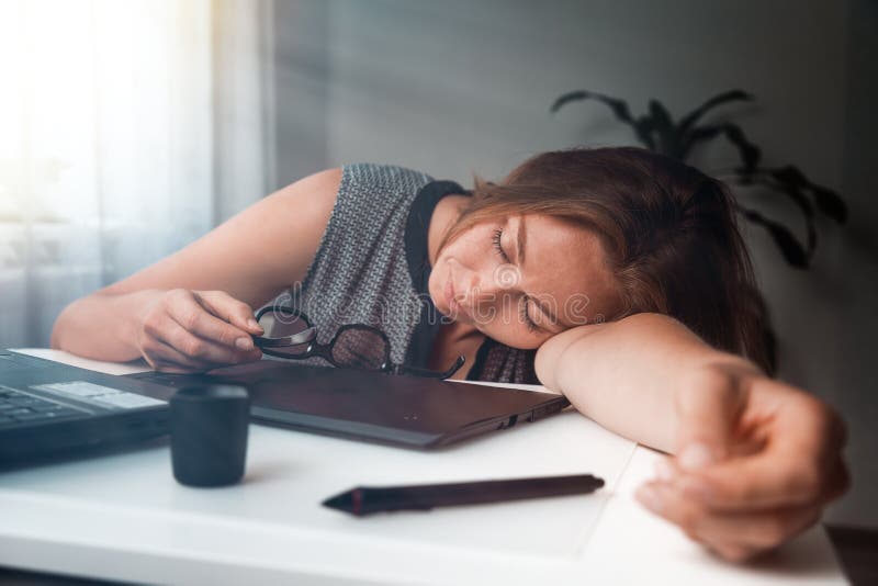 Jonge vrouw slaapt op het werk. Vermoeidheid en overbelasting op kantoorwerk. Het licht van de ochtend stock foto Jonge vrouw slaapt op het werk. Vermoeidheid en overbelasting op kantoorwerk. Het licht van de ochtend stock foto