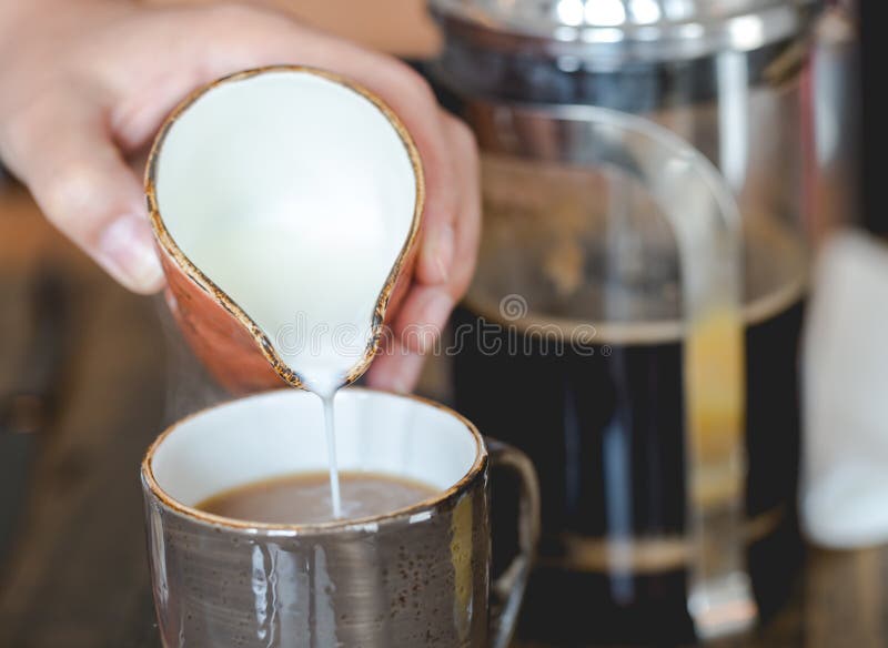Jonge vrouwen gietende melk in kop van gefiltreerde koffie stock afbeelding Jonge vrouwen gietende melk in kop van gefiltreerde koffie stock afbeelding