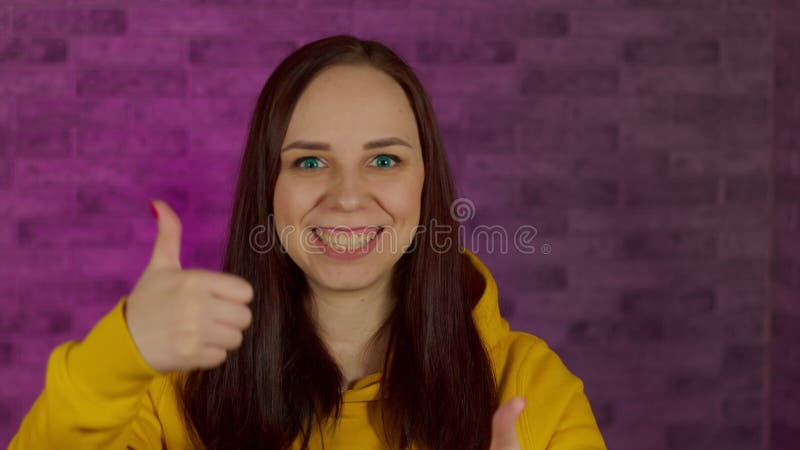 Jonge vrouwen glimlachen en duimen tonen op de achtergrond van een verlichte muur. close-up van vrolijke vrouw met gebaar van