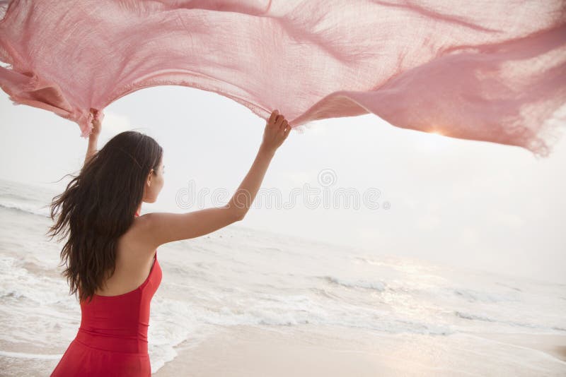 Jonge vrouwen op de sjaal van de strandholding in de lucht en het onderzoeken van de afstand stock afbeelding Jonge vrouwen op de sjaal van de strandholding in de lucht en het onderzoeken van de afstand stock afbeelding