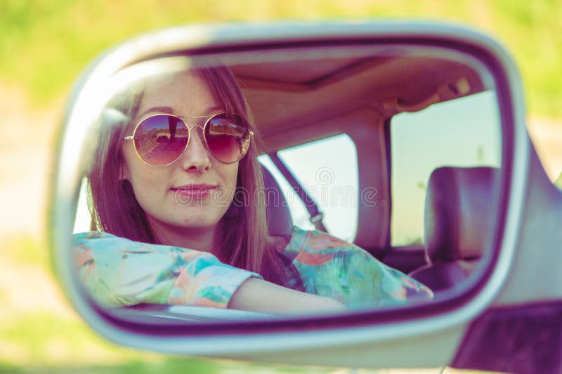 Jonge vrouwenbestuurder in de auto die aan de zijaanzichtspiegel kijken stock fotografie Jonge vrouwenbestuurder in de auto die aan de zijaanzichtspiegel kijken stock fotografie