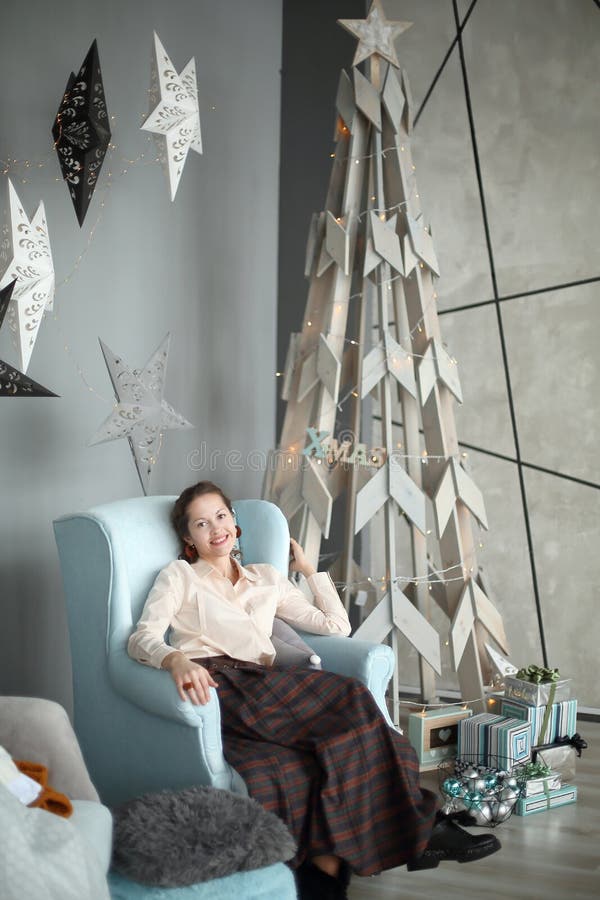 Jonge vrouwenzitting als voorzitter dichtbij een gestileerde Kerstboom royalty-vrije stock foto's Jonge vrouwenzitting als voorzitter dichtbij een gestileerde Kerstboom royalty-vrije stock foto's