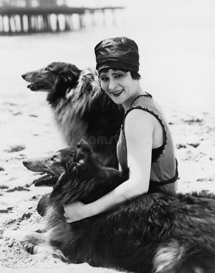 Jonge vrouwenzitting met haar Collies op het strand (Alle afgeschilderde personen leven niet langer en geen landgoed bestaat Leve stock foto Jonge vrouwenzitting met haar Collies op het strand (Alle afgeschilderde personen leven niet langer en geen landgoed bestaat Leve stock foto