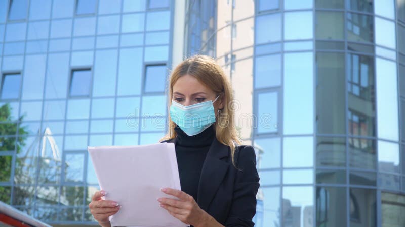 Jonge zakenvrouw in beschermende maskers met documenten op straat. mooie blonde documenten bekijken