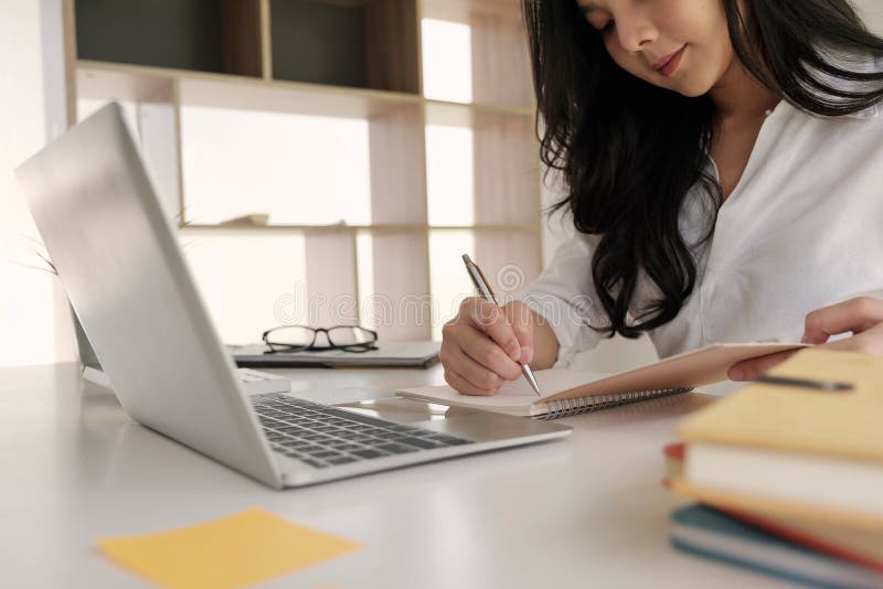 Young business woman taking notes in notebook.On table is laptop for online learning or business finance concept. Young business woman taking notes in notebook.On table is laptop for online learning or business finance concept.