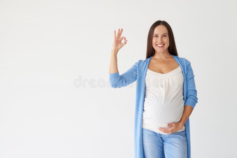 Jonge zwangere vrouw die o.k. die gebaar tonen op witte rug wordt geïsoleerd stock afbeelding Jonge zwangere vrouw die o.k. die gebaar tonen op witte rug wordt geïsoleerd stock afbeelding
