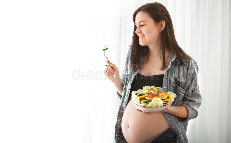 Jonge zwangere vrouw die salade thuis eten royalty-vrije stock fotografie Jonge zwangere vrouw die salade thuis eten royalty-vrije stock fotografie