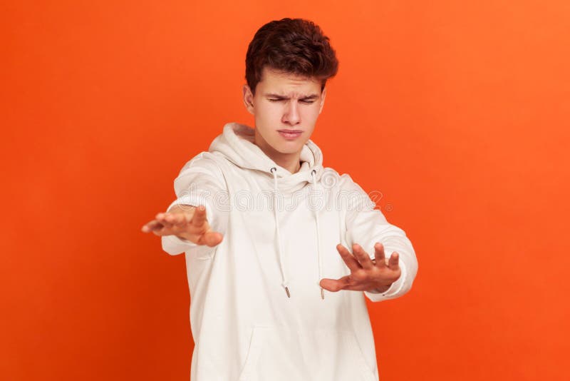 Young man in casual style hoodie standing with closed eyes and forward outstretched arms, disoriented in space teenager, blindness. Indoor studio shot isolated on orange background. Young man in casual style hoodie standing with closed eyes and forward outstretched arms, disoriented in space teenager, blindness. Indoor studio shot isolated on orange background