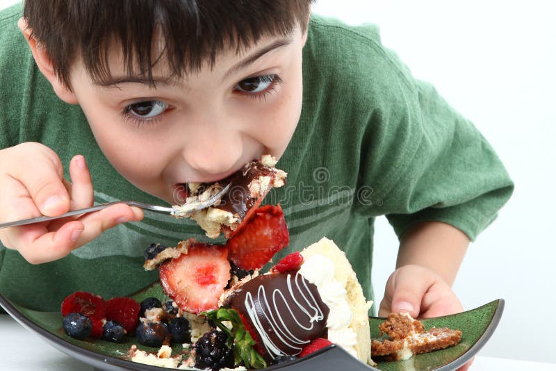 Adorable six year old boy eating glazed fruit cheesecake. Adorable six year old boy eating glazed fruit cheesecake.