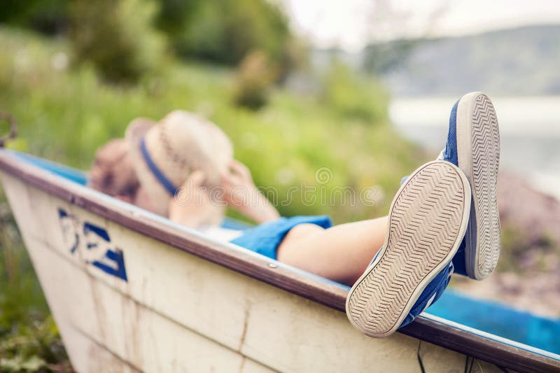 Jongen die in oude boot in het beeld van de meerkust dicht omhoog liggen stock fotografie Jongen die in oude boot in het beeld van de meerkust dicht omhoog liggen stock fotografie