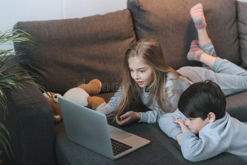 Jongen en meisje die laptop op bank samen met behulp van stock foto's Jongen en meisje die laptop op bank samen met behulp van stock foto's