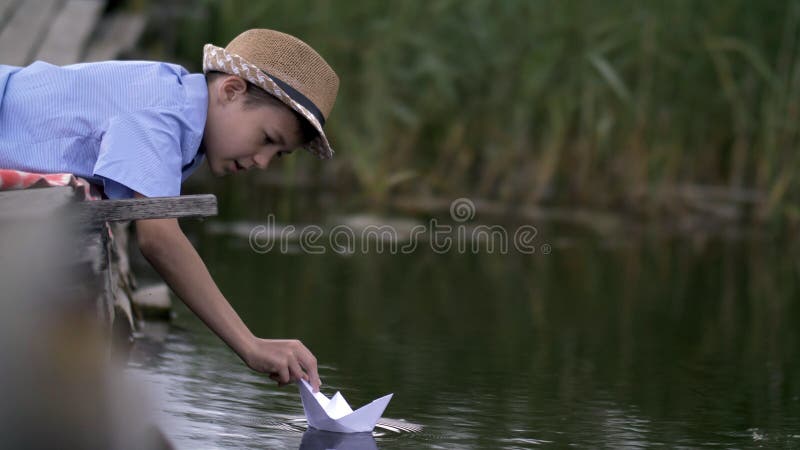 Jongen het spelen met een document boot in het meer op de pijler royalty-vrije stock afbeelding Jongen het spelen met een document boot in het meer op de pijler royalty-vrije stock afbeelding