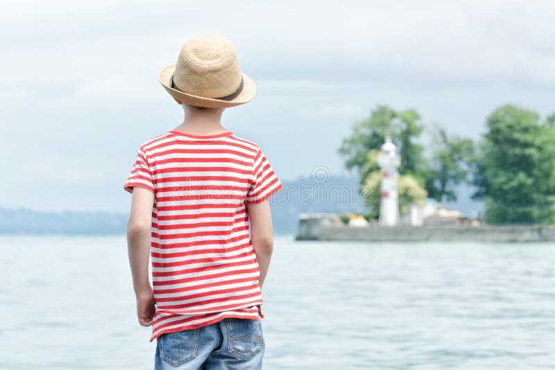 Jongen in hoed die zich op het strand bevinden Kleine vuurtoren in distan stock afbeelding Jongen in hoed die zich op het strand bevinden Kleine vuurtoren in distan stock afbeelding