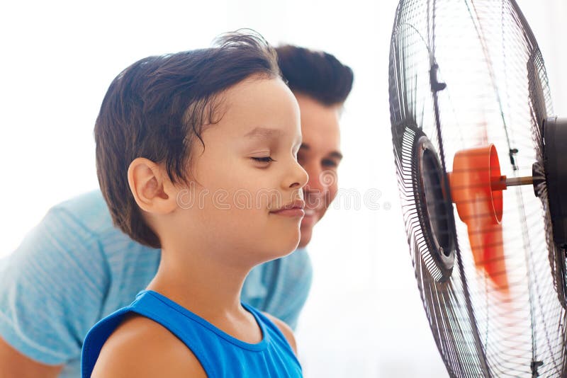 Jongen met zijn papa die voor ventilator koelen royalty-vrije stock fotografie Jongen met zijn papa die voor ventilator koelen royalty-vrije stock fotografie