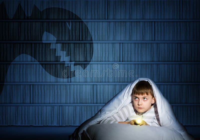 Image of a boy under the covers with a flashlight the night afraid of ghosts. Image of a boy under the covers with a flashlight the night afraid of ghosts