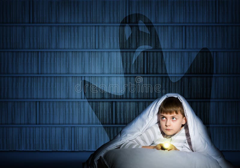 Image of a boy under the covers with a flashlight the night afraid of ghosts. Image of a boy under the covers with a flashlight the night afraid of ghosts