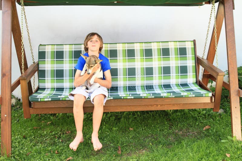 Jongenszitting op een tuinschommeling met hond stock foto Jongenszitting op een tuinschommeling met hond stock foto