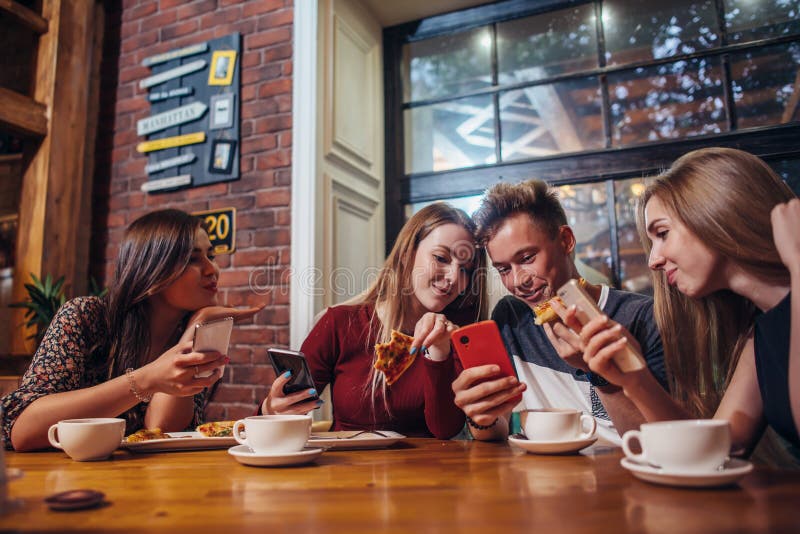 Jongeren die hun mobiele telefoons met behulp van die de lijst rondhangen die een maaltijd in moderne modieuze koffie hebben royalty-vrije stock foto's Jongeren die hun mobiele telefoons met behulp van die de lijst rondhangen die een maaltijd in moderne modieuze koffie hebben royalty-vrije stock foto's