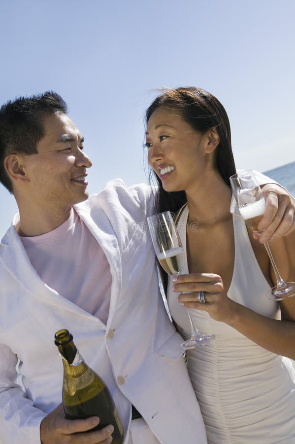 Happy newlywed couple with champagne bottle and flutes looking at each on beach. Happy newlywed couple with champagne bottle and flutes looking at each on beach