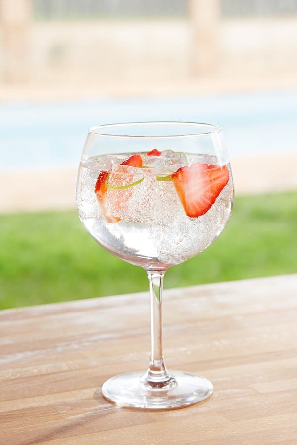 Jordgubbegin- och uppiggningsmedelcoctail vid en pöl utomhus royaltyfria bilder Jordgubbegin- och uppiggningsmedelcoctail vid en pöl utomhus royaltyfria bilder